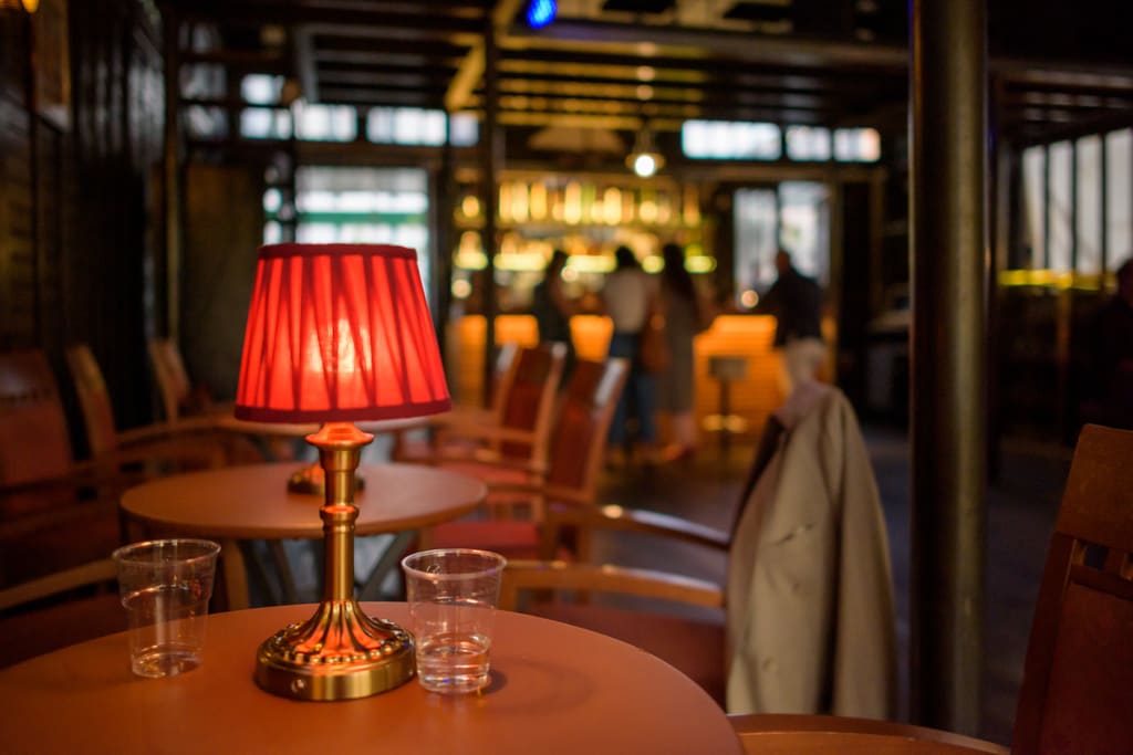 Tavolino con lampada dal paralume rosso, il bar sullo sfondo